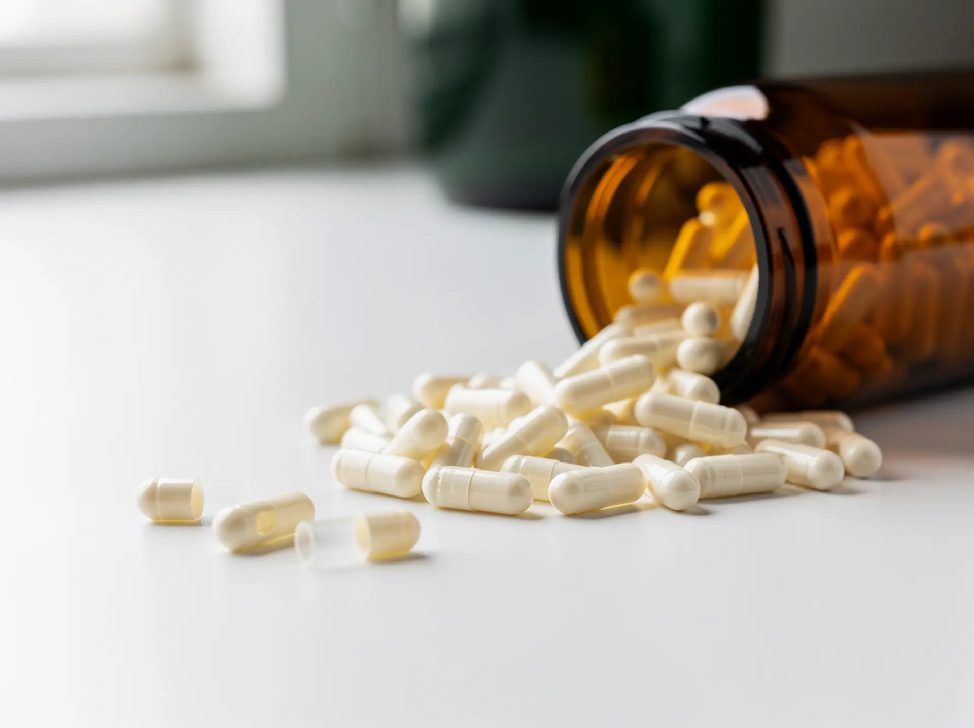 Empty ivory-white two-piece acid-resistant HPMC hard capsules spilling from a tilted amber glass jar