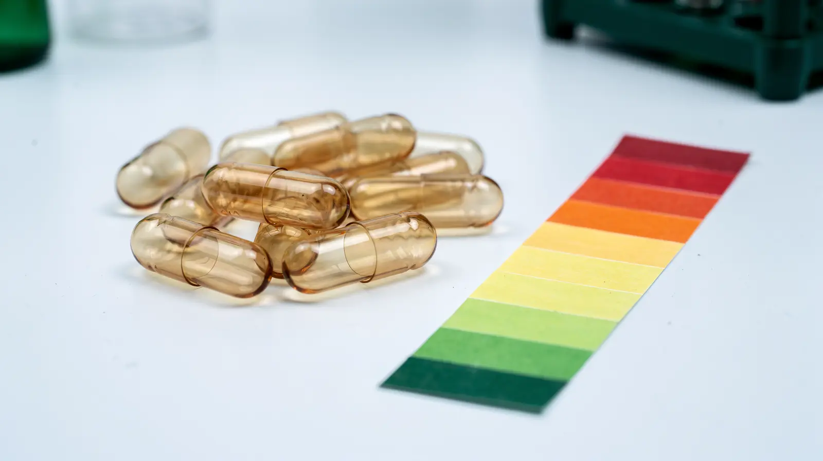 Empty transparent acid-resistant hard capsule shells beside pH indicator strips